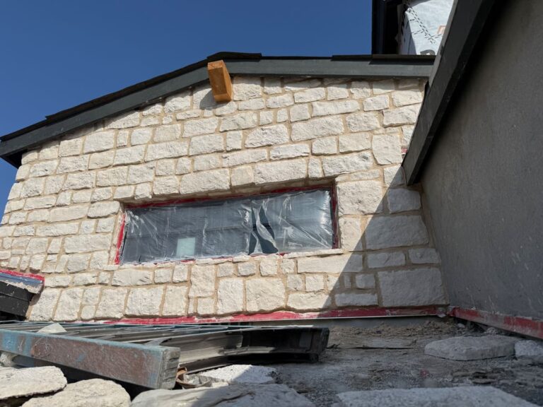 Light-colored natural stone veneer being installed on a residential exterior wall during a home remodel.