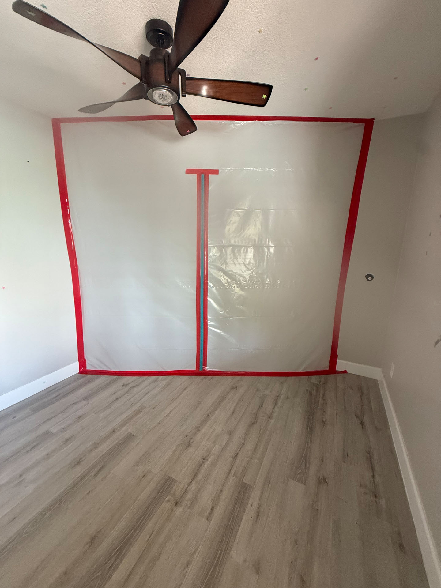 Plastic sheeting barrier with red tape seals off a construction zone in a room with laminate floors.