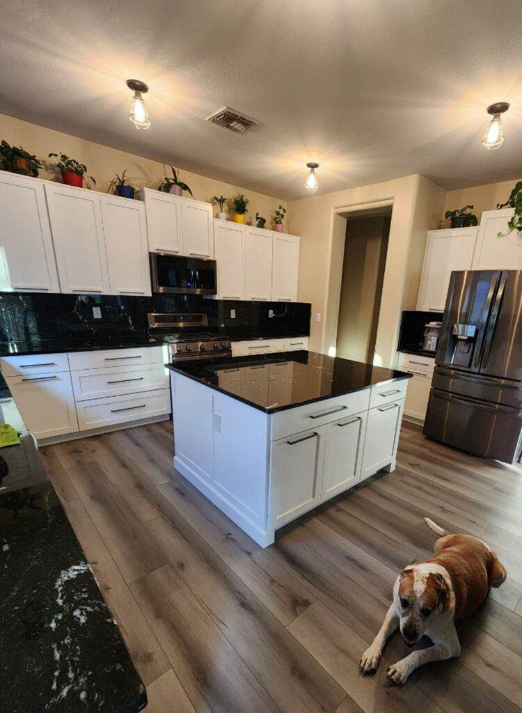 A modern kitchen renovation featuring white shaker cabinets, black granite countertops, and wood-look flooring.