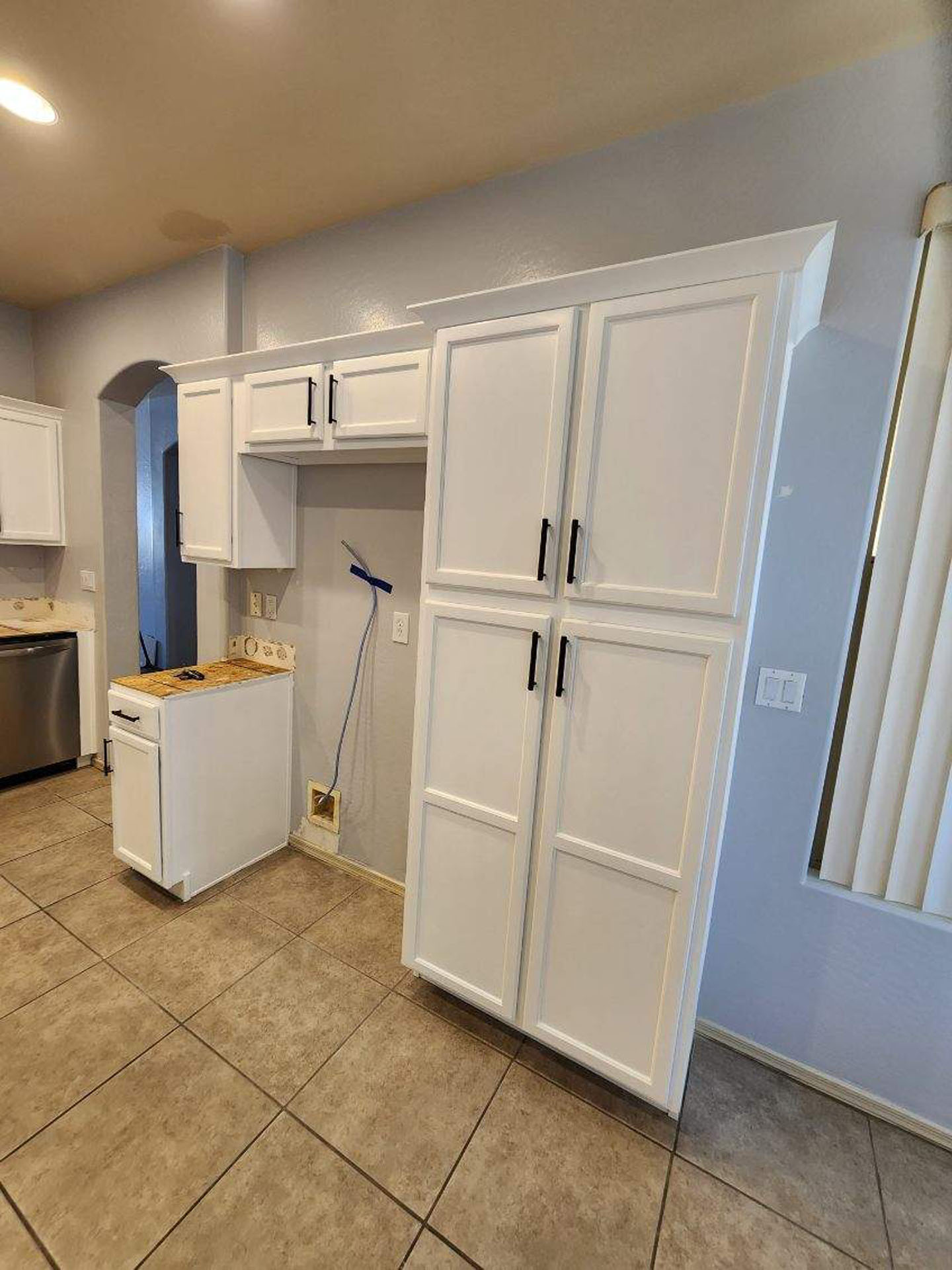 Modern floor-to-ceiling white shaker pantry cabinet with black hardware in a kitchen renovation.