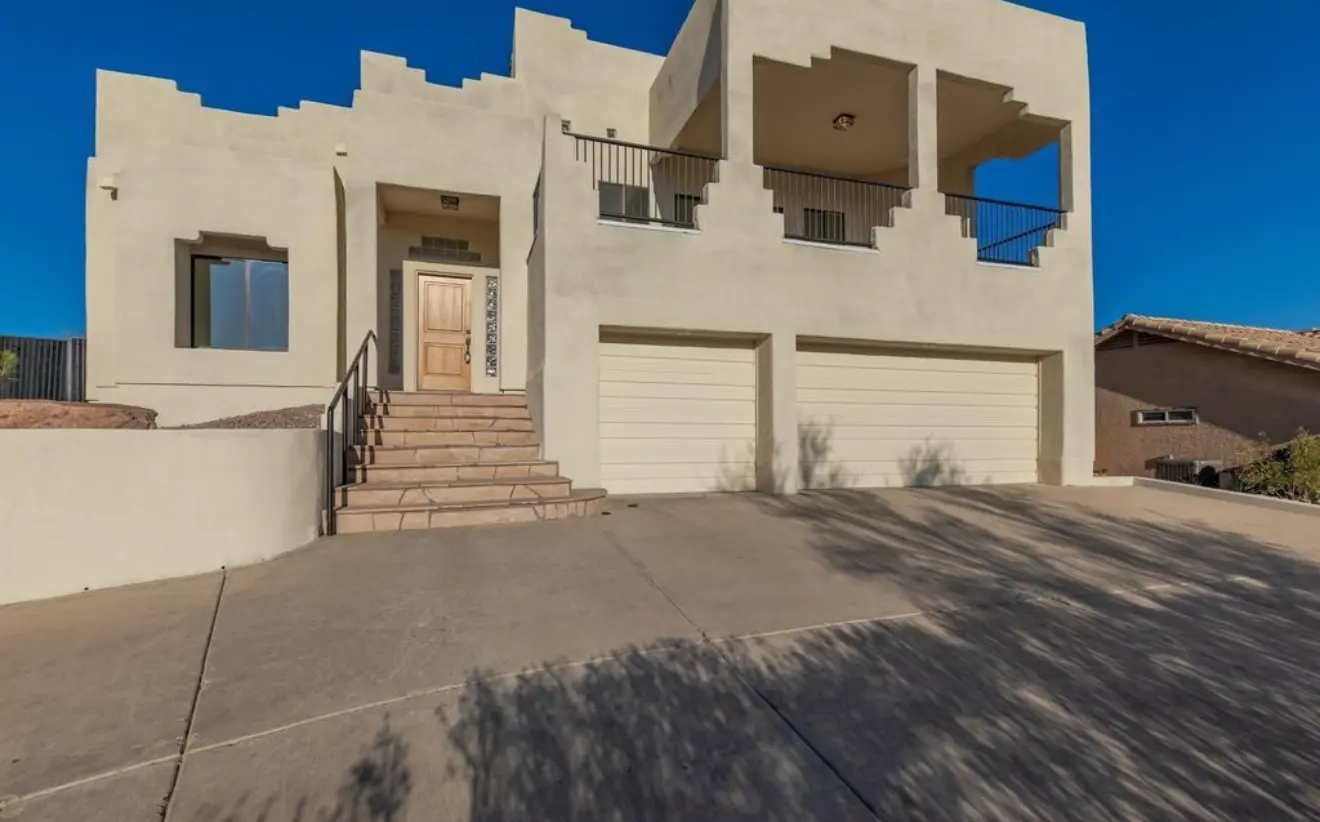 A multi-level Southwestern style home with beige stucco walls, two-car garage, and stone entrance stairs.