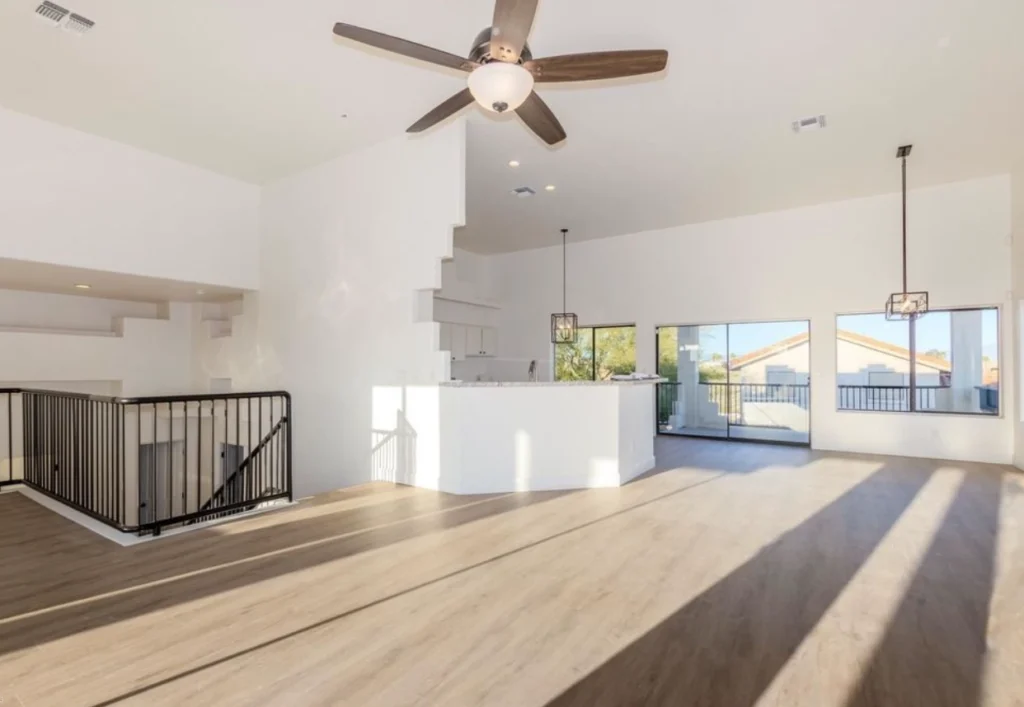 Modern open-concept living room with light wood flooring, white walls, and black metal staircase railing.