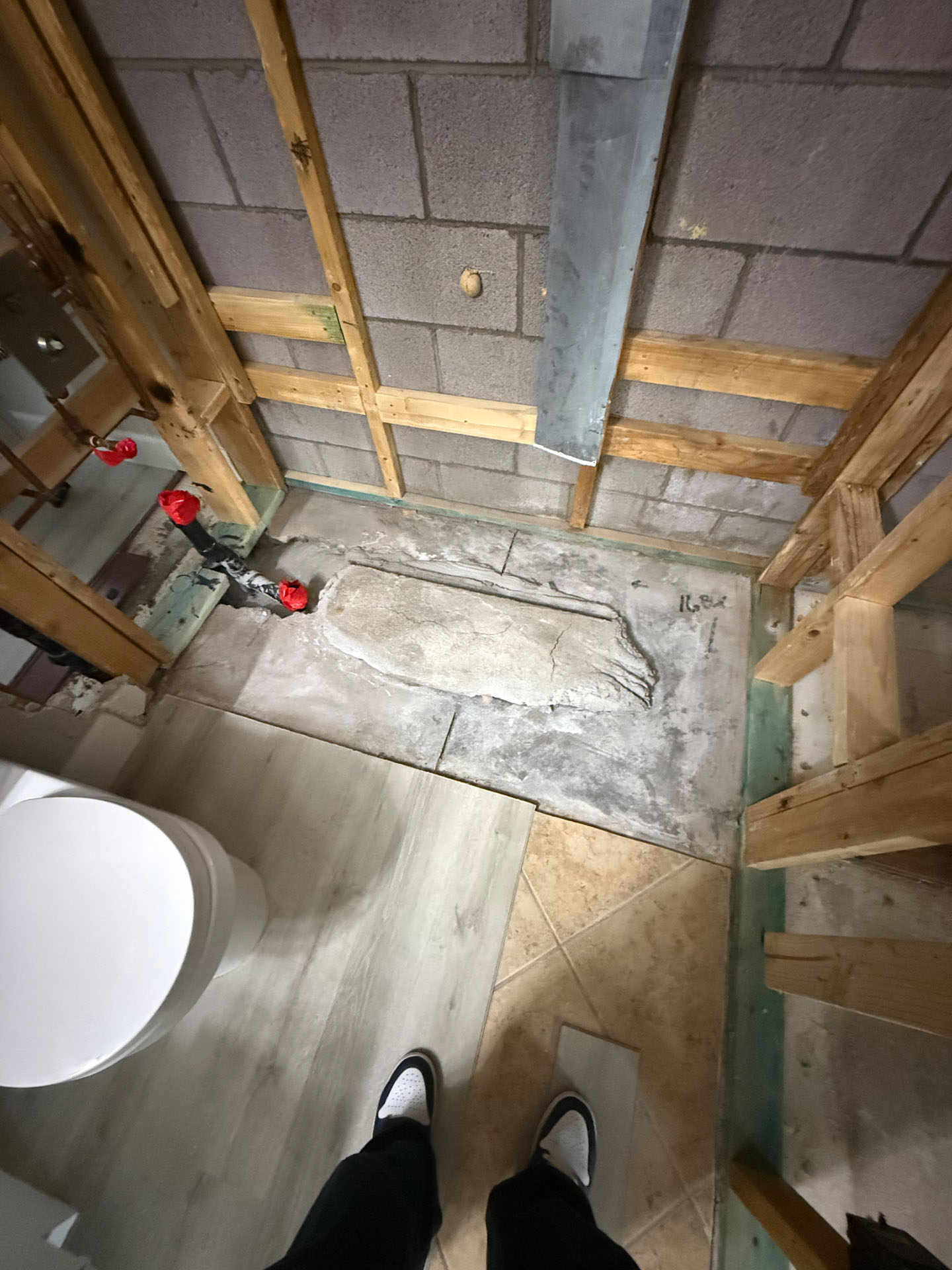 Bathroom renovation site showing exposed wood wall framing, concrete floors, and capped plumbing pipes.