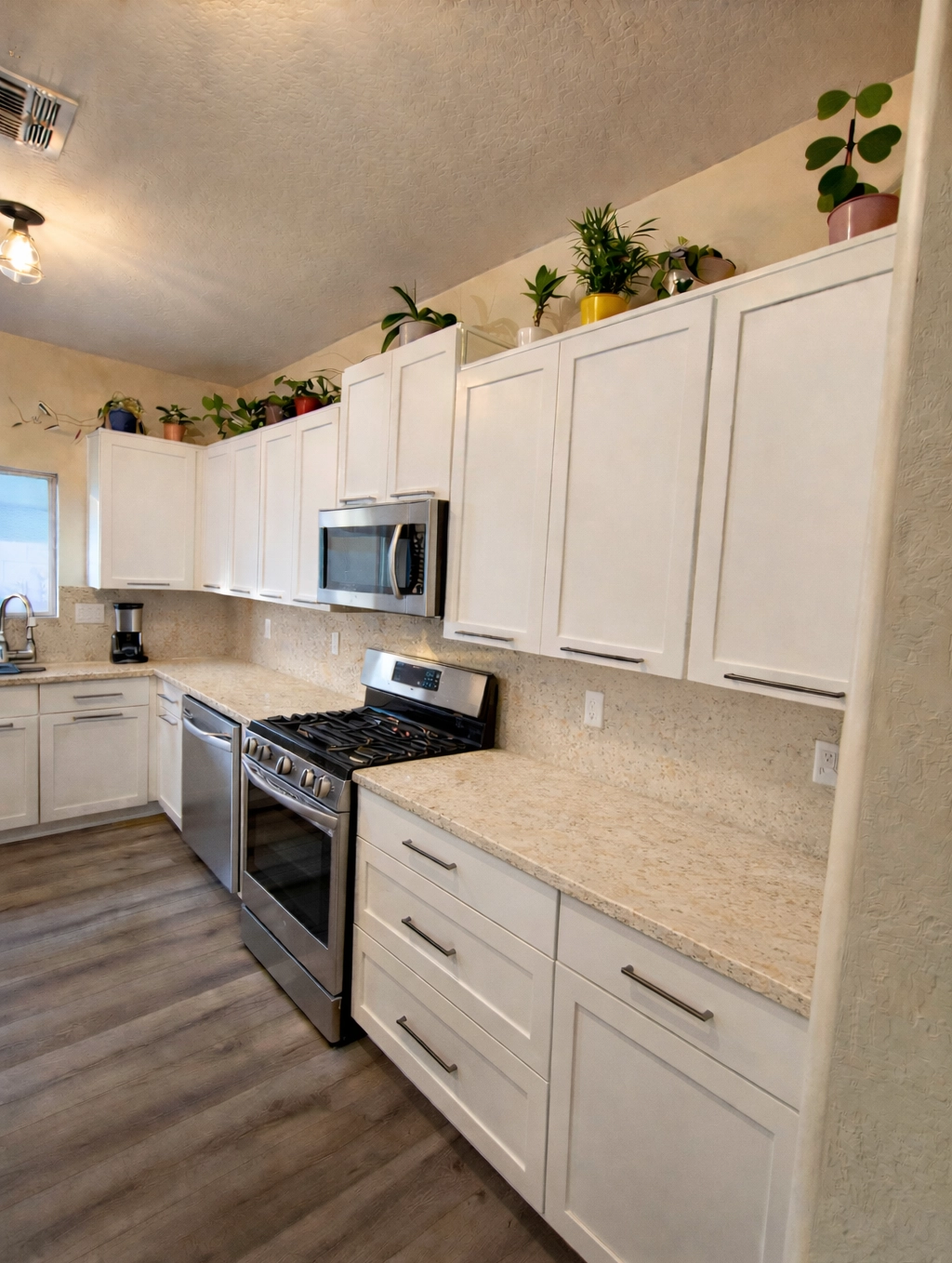 Modern kitchen featuring white shaker cabinets, light granite countertops, stainless steel gas range, and indoor plants.