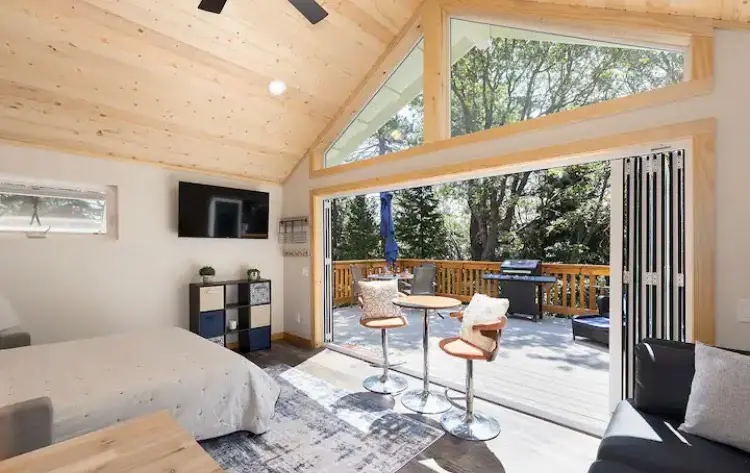 Interior view of a modern bedroom with a vaulted wood ceiling and bi-fold doors opening to a scenic wooden deck.