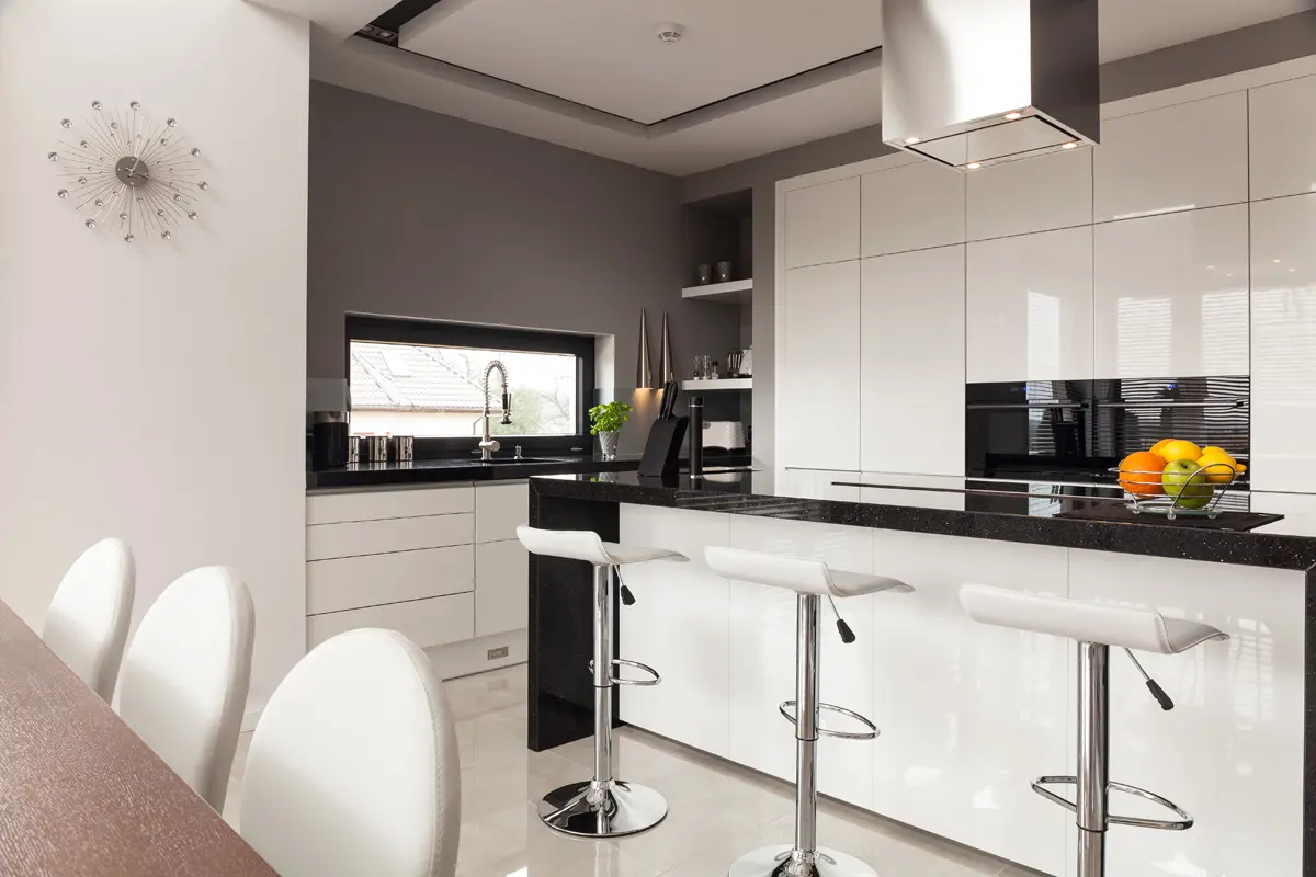 Modern kitchen interior with white gloss cabinets, black granite breakfast bar, and stylish white bar stools.